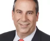 Person in a suit with a red tie, smiling against a white background.