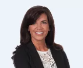 Person smiling in a black blazer against a light background.