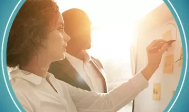 Two individuals brainstorming with sticky notes on a board, sunlight streaming through the window.