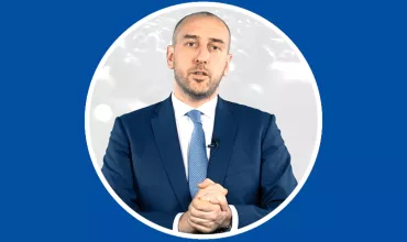 Person in a suit speaking with a blue background.