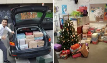 Car trunk filled with wrapped presents, person smiling beside it.