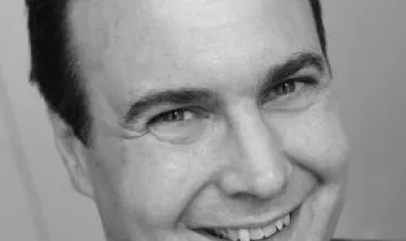 A person smiling in a professional portrait, black and white.