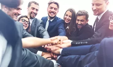 Group of people in business attire joining hands in a team huddle.