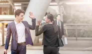 Deux personnes en costume se saluant d'un high five devant un bâtiment de bureaux.