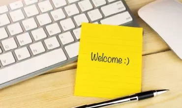 Note jaune avec 'Welcome :)' à côté d'un clavier et stylo.
