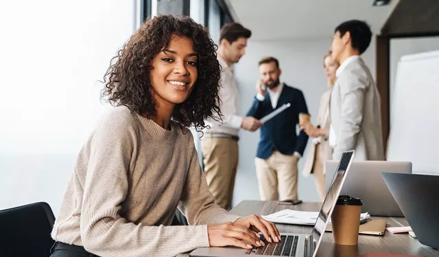 Person smiling, working on a laptop in a group setting.